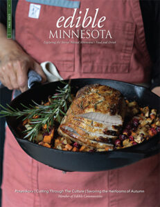 Edible Minnesota magazine front cover of Fall 2023 issue. Pot roast in cask iron pans held by woman in a red apron